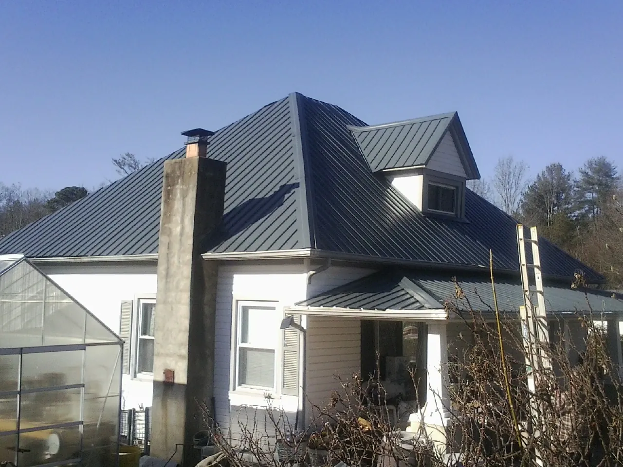 Dark blue standing seam metal roof on a white farmhouse with dormer — Slate & Tile Roof Repair by Roofing Brothers in Thompsons Station