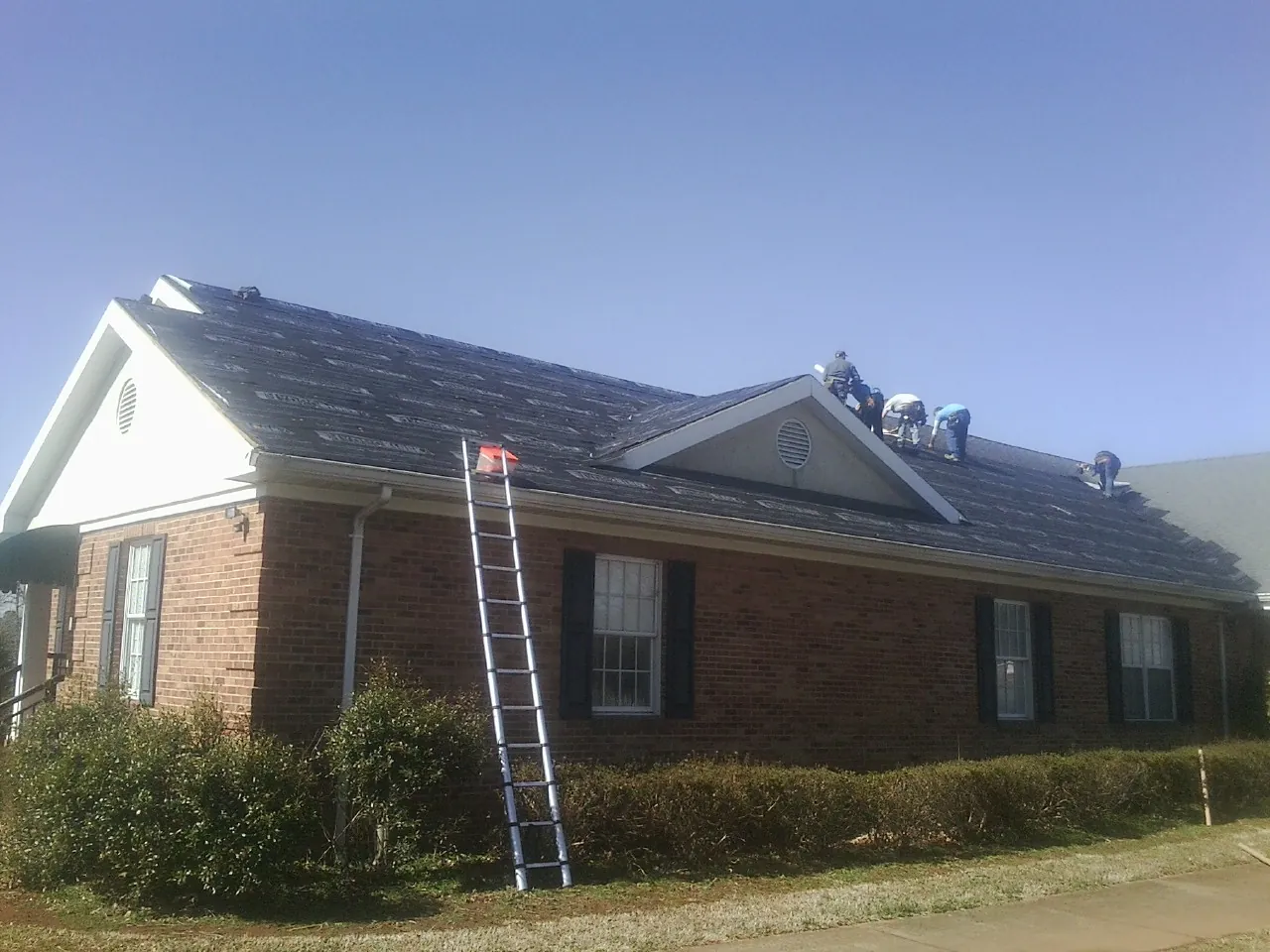 Crew tearing shingles off a brick ranch roof with a ladder set — Metal Roof Repair work by our crew in Thompsons Station