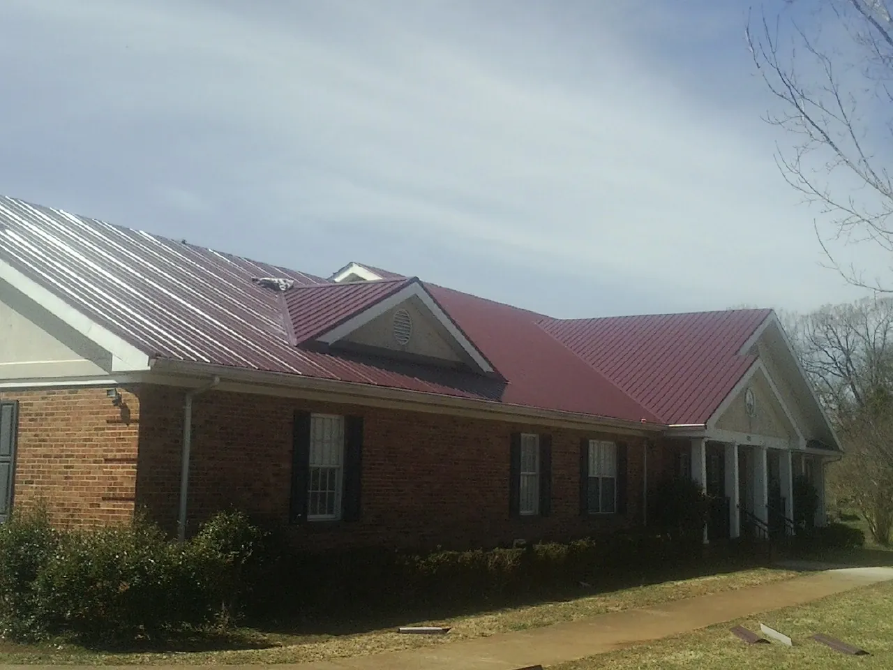 Red metal roof with gabled entries on a long brick building, from a Hail Damage Roof Repair job in Thompsons Station