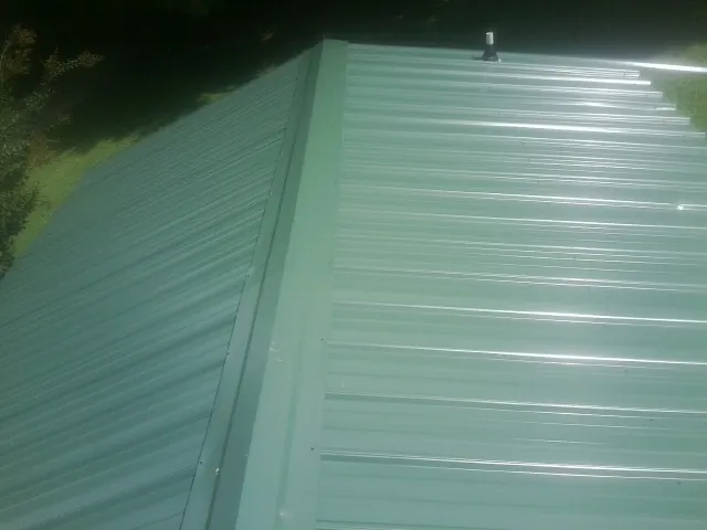 New green metal panels meeting at the ridge of a roof — Flat Roof Repair work by our crew in Thompsons Station