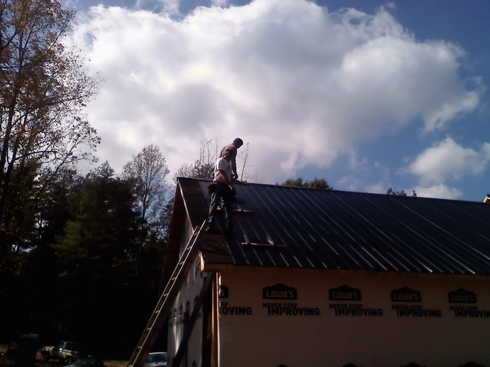 Roofer fastening dark metal panels high against a cloudy sky, from a Roof Inspection job in Thompsons Station