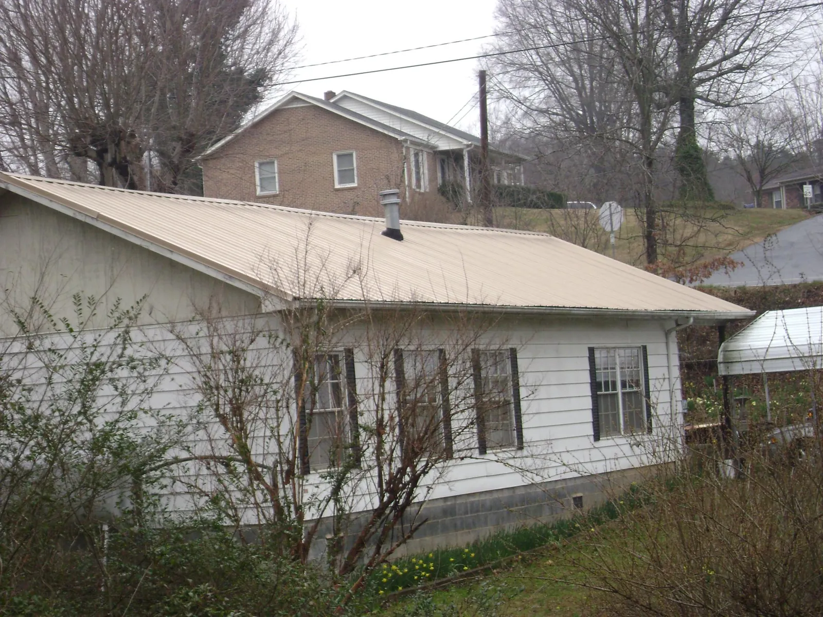 Tan metal roof on a white sided house set into a hillside — Commercial Roofing by Roofing Brothers in Thompsons Station